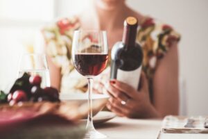 Woman looking at wine bottle while glass of wine sits in front of her